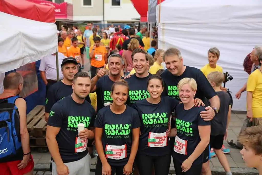 Rollo Solar Team beim Lauf, alle tragen schwarze T-Shirts mit grüner Beschriftung, im Hintergrund sind viele Teilnehmer und Zelte zu sehen.