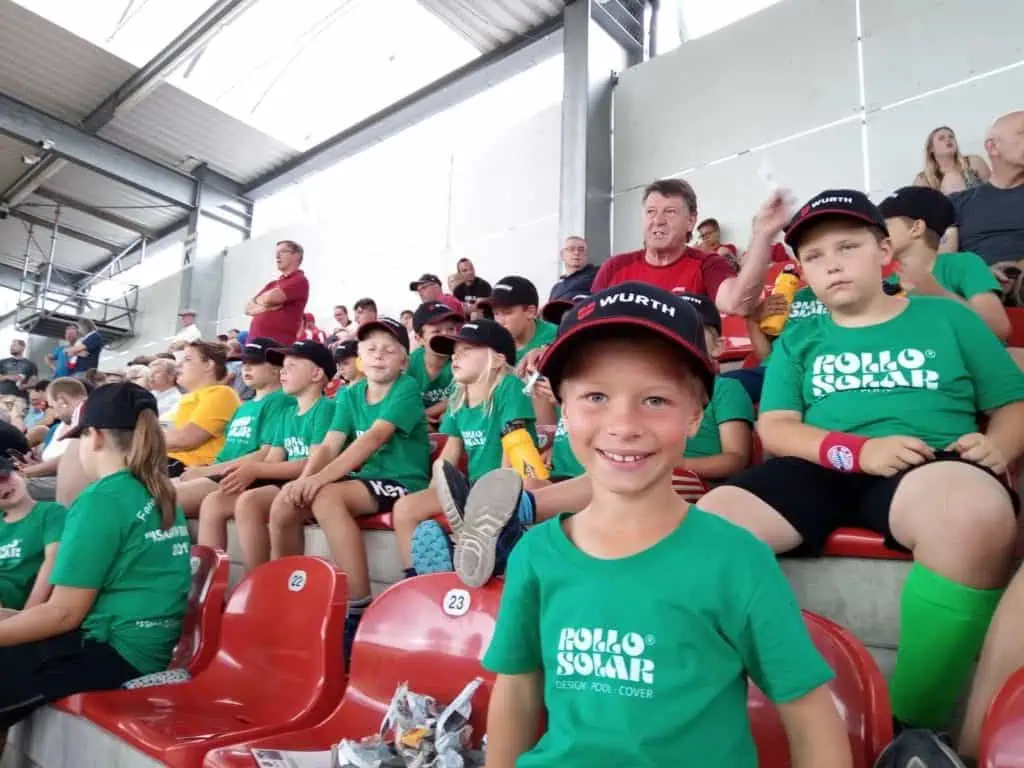 Hochwertiges Kind mit grüner Rollo Solar Trikot, lächelnd im Stadion, im Fokus auf das Engagement und die Qualität deutscher Poolabdeckungen.